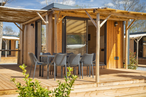 Udendørs træterrasse med spisebord og seks stole foran et moderne træhus på Beach Resort «Agde 5» i Frankrig.