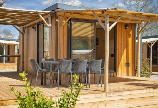 Udendørs træterrasse med spisebord og seks stole foran et moderne træhus på Beach Resort «Agde 5» i Frankrig.
