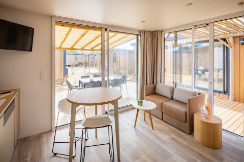 Moderne opholdsstue i Beach Resort «Agde 5», Frankrig, med stor glasdør til terrasse og udendørs spiseplads.