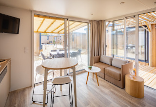 Moderne opholdsstue i Beach Resort «Agde 5», Frankrig, med stor glasdør til terrasse og udendørs spiseplads.