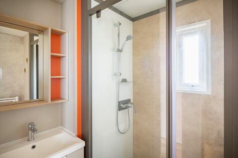Moderne glampingbadeværelse med bruseniche, håndvask, spejl og naturligt lys fra et lille vindue.