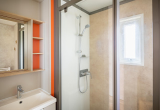 Moderne glampingbadeværelse med bruseniche, håndvask, spejl og naturligt lys fra et lille vindue.