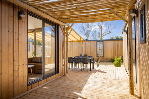 Træterrasse ved Beach Resort «Agde 5» i Frankrig med udendørs spiseområde, sollys og moderne lodge.