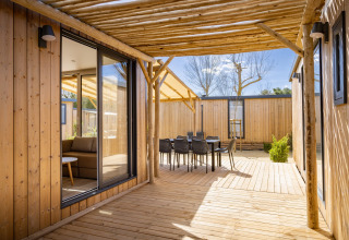 Træterrasse ved Beach Resort «Agde 5» i Frankrig med udendørs spiseområde, sollys og moderne lodge.