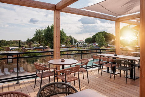 Terrasse med træmøbler og udsigt over glamping-område, træer og hytter i aftensolens skær.