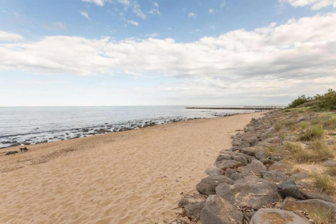 Udsigt over en fredelig sandstrand med klipper og græs, taget fra et glamping-sted ved havet.