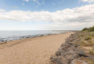 Udsigt over en fredelig sandstrand med klipper og græs, taget fra et glamping-sted ved havet.