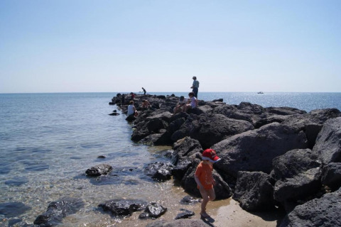 Folk nyder solen på store klipper ved havet ved et glampingsted med en klar blå himmel og roligt vand.