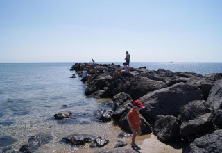 Folk nyder solen på store klipper ved havet ved et glampingsted med en klar blå himmel og roligt vand.