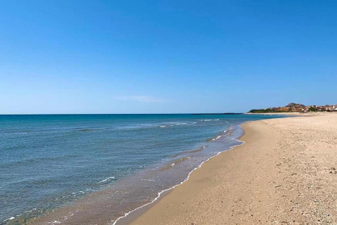 Rolig strand med blåt hav og sand, set fra et glampingophold under en klar blå himmel, ingen mennesker.