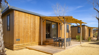Vista exterior de una casa móvil en Beach Resort Agde 4 con terraza de madera, pérgola y muebles de exterior.