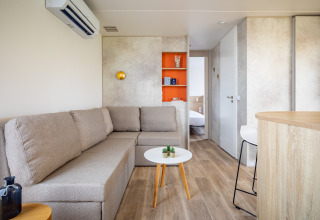 Lyst mobilhjems stue med beige sofa, bord og orange reol på Beach Resort Agde 4 i Frankrig.