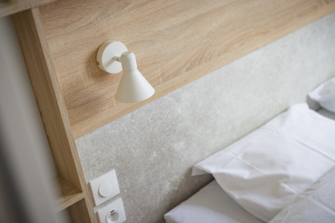 Moderne soveværelsesdetaljer med seng, væglampe og kontakt i Beach Resort «Agde 4», Frankrig.