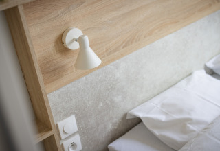 Moderne soveværelsesdetaljer med seng, væglampe og kontakt i Beach Resort «Agde 4», Frankrig.
