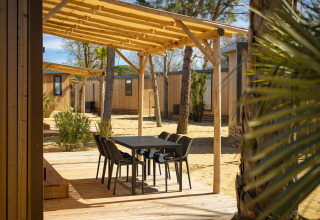Udendørs terrasse med sort bord og stole under træpergola ved Beach Resort «Agde 4» i Frankrig.