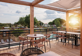 Udendørs terrasse med træmøbler og udsigt over mobilhome-området, omgivet af træer og solnedgang.