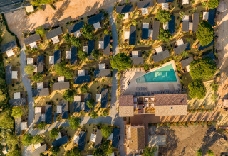 Luftfoto af mobilhome-park med mange små hytter, træer og en stor swimmingpool i centrum.