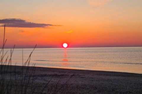 Solnedgang over havet set fra stranden ved en mobilhome, himlen gløder i orange og røde nuancer.