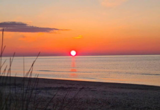 Solnedgang over havet set fra stranden ved en mobilhome, himlen gløder i orange og røde nuancer.