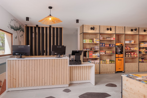 Modern reception og butik med træindretning og snacks på hylderne i Beach Resort Agde 2, Frankrig.