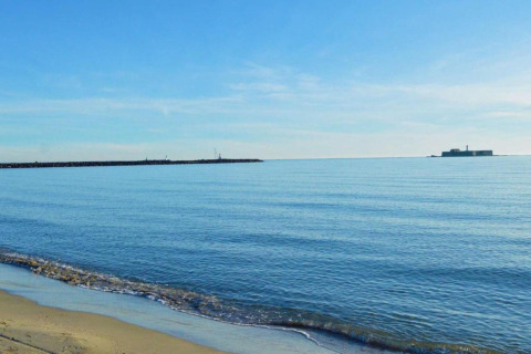 Billede af rolig sandstrand og klart hav ved Beach Resort «Agde 2» i Frankrig, med en bygning i horisonten.