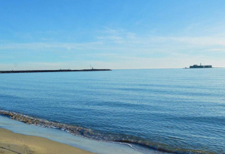 Billede af rolig sandstrand og klart hav ved Beach Resort «Agde 2» i Frankrig, med en bygning i horisonten.