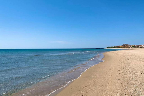 Udsigt over en tom sandstrand og roligt hav ved Beach Resort «Agde 2» i Frankrig, under en klar blå himmel.