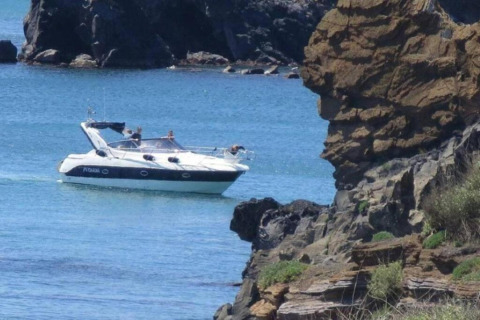 En motorbåd sejler tæt på klipperne ved Beach Resort «Agde 2» i Frankrig, omgivet af blåt havvand.