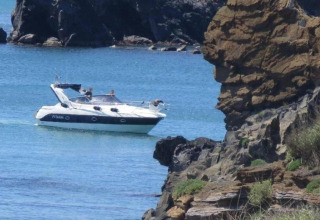 En motorbåd sejler tæt på klipperne ved Beach Resort «Agde 2» i Frankrig, omgivet af blåt havvand.