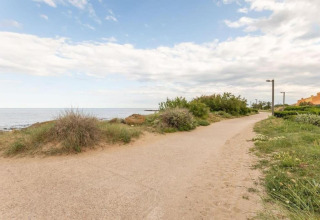 Sti ved stranden ved Beach Resort «Agde 2» i Frankrig, omgivet af grønne buske og udsigt til havet.