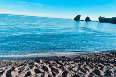 Udsigt over stranden og det rolige blå hav ved Beach Resort «Agde 2» i Frankrig, med klippeformationer i horisonten.