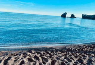 Udsigt over stranden og det rolige blå hav ved Beach Resort «Agde 2» i Frankrig, med klippeformationer i horisonten.