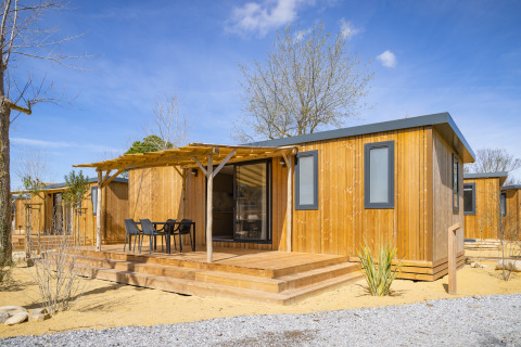 Moderne mobilhome i træ med terrasse og havemøbler ved Beach Resort Agde 1 under blå himmel.