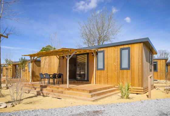 Moderne mobilhome i træ med terrasse og havemøbler ved Beach Resort Agde 1 under blå himmel.