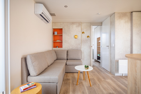 Moderne stue i mobilhome Beach Resort «Agde 1» i Frankrig med hjørnesofa, bord og hyggelig indretning.