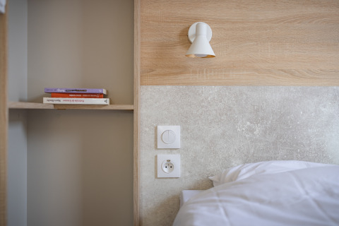 Moderne mobilhomesoveværelse med træpanel, seng, hylde med bøger og væglampe på Beach Resort Agde 1.