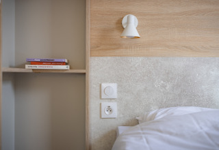 Moderne mobilhomesoveværelse med træpanel, seng, hylde med bøger og væglampe på Beach Resort Agde 1.