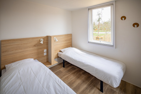 Moderne mobilhome-soveværelse med to enkeltsenge, lyse vægge og stort vindue i Beach Resort Agde 1, Frankrig.