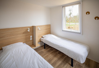 Moderne mobilhome-soveværelse med to enkeltsenge, lyse vægge og stort vindue i Beach Resort Agde 1, Frankrig.