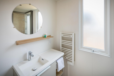Moderne badeværelse i mobilhome Beach Resort «Agde 1» i Frankrig med spejl, håndvask og vindue.