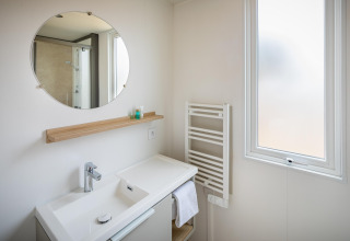 Moderne badeværelse i mobilhome Beach Resort «Agde 1» i Frankrig med spejl, håndvask og vindue.