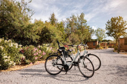 To cykler står på en grusvej foran mobilhjem og blomstrende buske på Beach Resort Agde 1 i Frankrig.