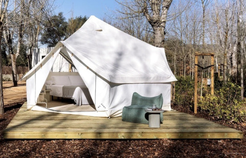 Safari tent Bell Tent Plus met witte canvas, houten terras en buitenzitje tussen de bomen.