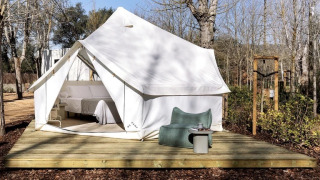Tente safari Bell Tent Plus avec toile blanche, terrasse en bois et coin détente extérieur en forêt.