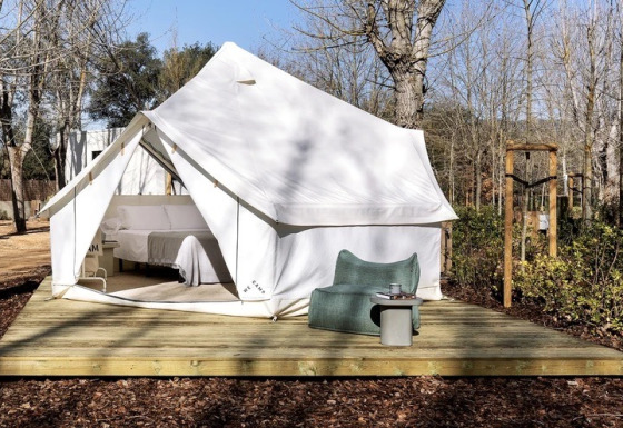 Safari tent Bell Tent Plus met witte canvas, houten terras en buitenzitje tussen de bomen.