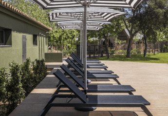 Sun loungers and striped umbrellas on wooden deck beside Cabin Tent at wecamp Santa Cristina, Spain.