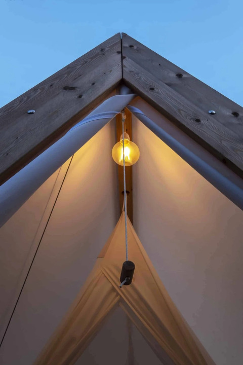 Binnenzicht van Cabin Tent met verlichte lamp bij Wecamp Santa Cristina, Spanje, bij valavond.