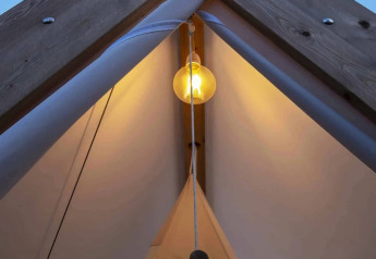 Interior view of Cabin Tent with glowing bulb at Wecamp Santa Cristina, Spain, during twilight.
