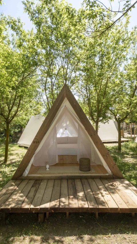 Safari Cabin Tent op houten terras in een groene bosomgeving, met open ingang en wit interieur.