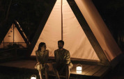 Two people sitting outside a lit safari cabin tent at night at Wecamp Santa Cristina in Spain.